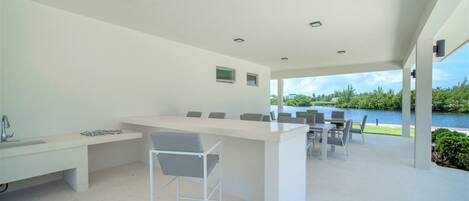 Un espace cuisine extérieur moderne, doté d’un bar, de sièges et offrant une vue sur un lac.