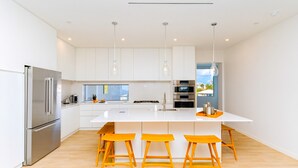 A modern kitchen with white cabinets, stainless steel appliances, a central island with bar stools, and pendant lighting. - Cayman Luxury Rentals at One Canal Point (Seven Mile Beach)