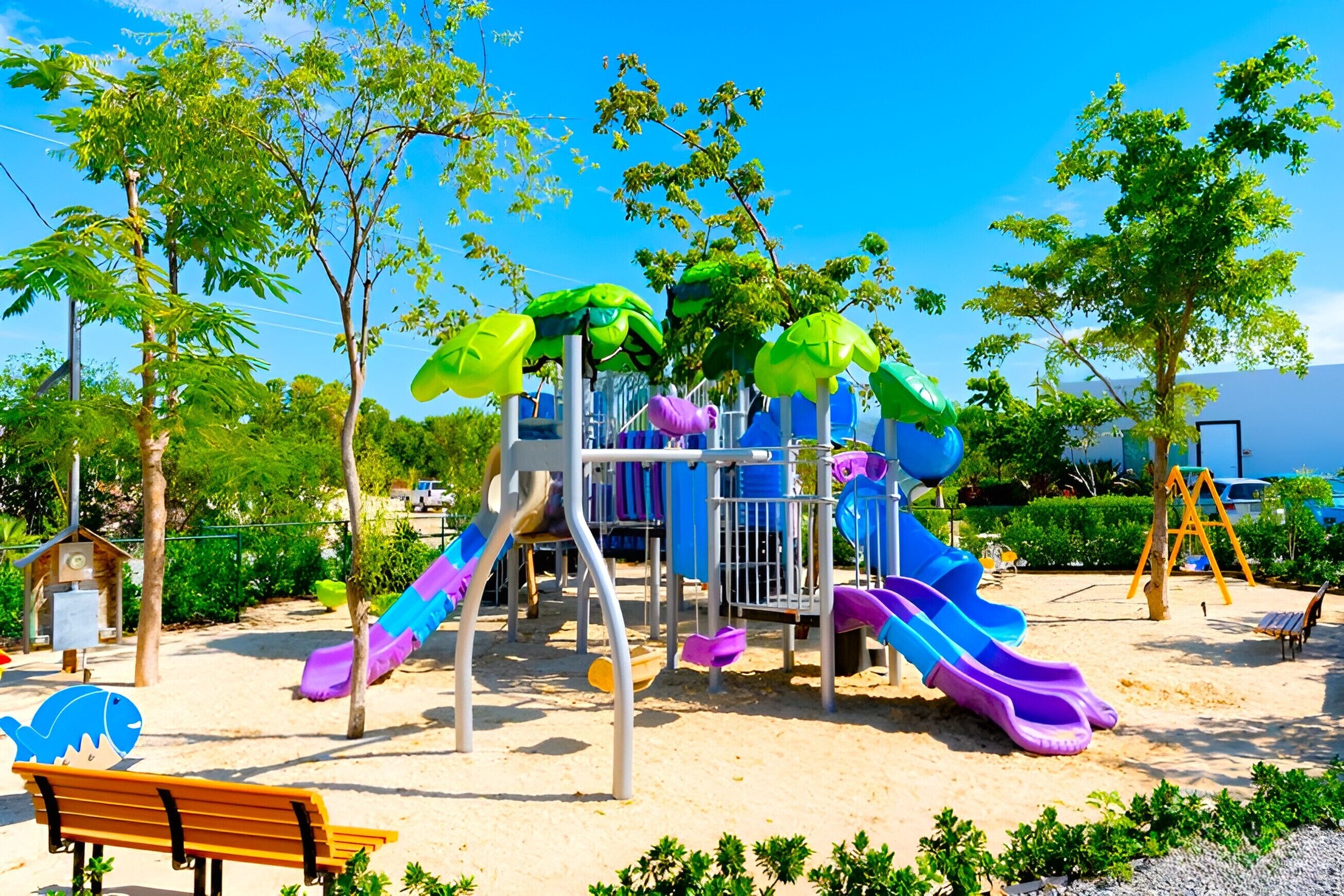 Un parque infantil con toboganes y estructuras para escalar, rodeado de árboles y bancos.