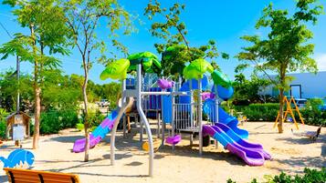 Un parque infantil con toboganes y estructuras para escalar, rodeado de árboles y bancos.