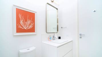 Casa de banho com uma pia branca, um espelho, uma obra de arte emoldurada e uma sanita.