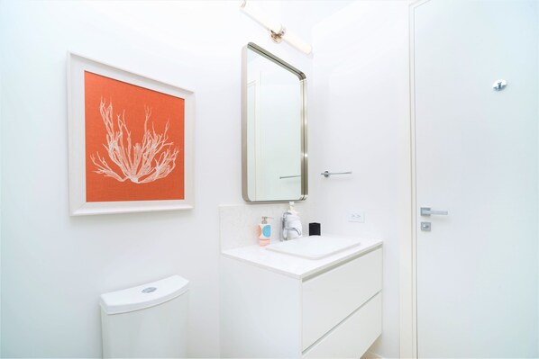 A bathroom with a white sink, a mirror, a framed artwork, and a toilet.