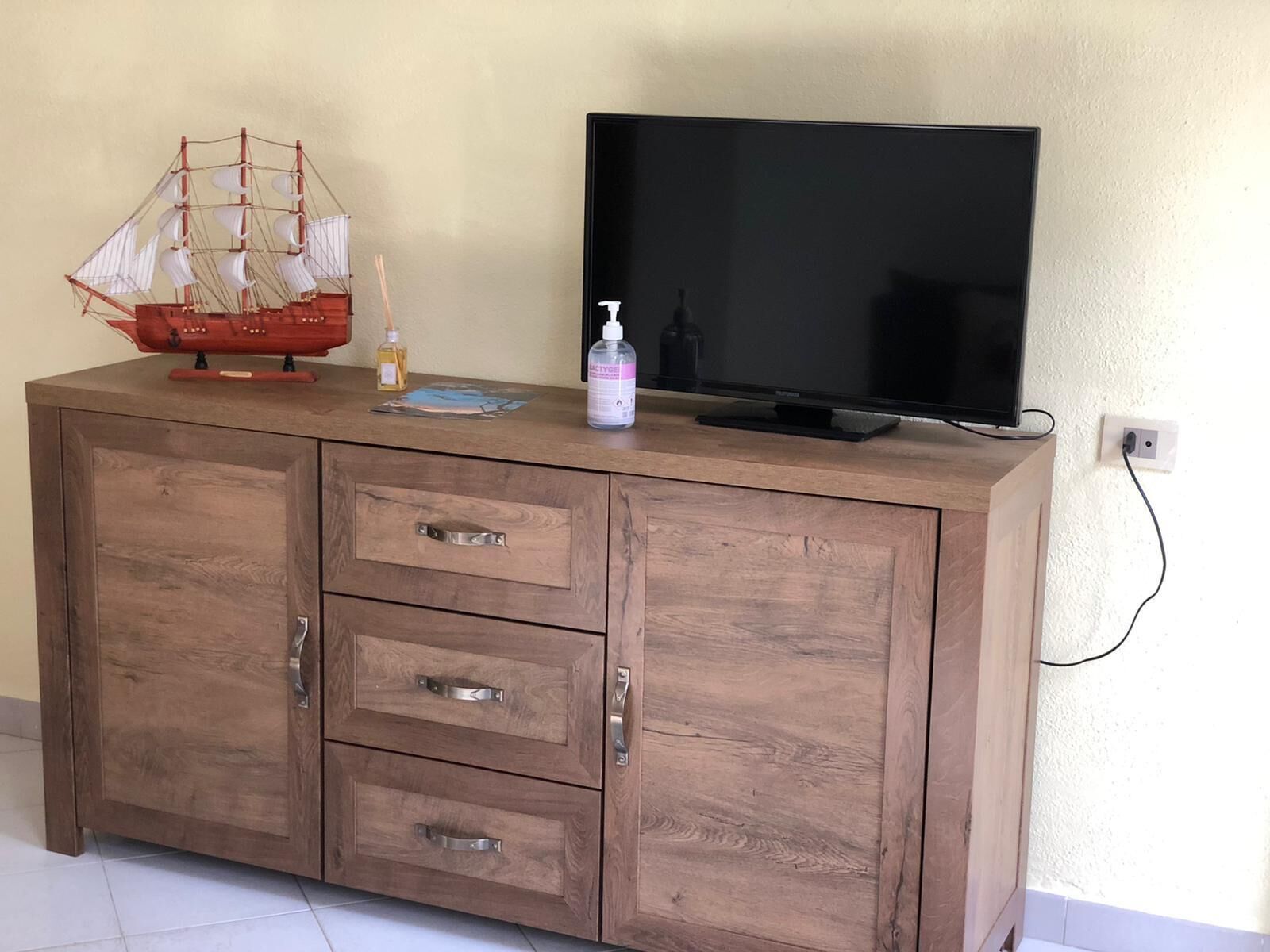 A wooden cabinet with three drawers and a television on top.