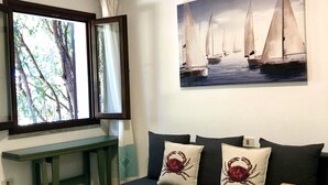 Quarto com sofá verde escuro, duas almofadas com tema de caranguejo, mesa de madeira e pintura de veleiros na parede.