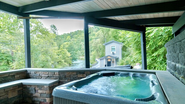A hot tub area with stone seating and a view of a house through a covered deck. - PENN STATE Country Creek Cottage w/ Hot Tub - ON Spring Creek and 7 miles to PSU (Bellefonte)