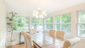 A dining room with a wooden table, four upholstered chairs, a hanging light fixture, and large windows with a view of greenery. - PENN STATE Country Creek Cottage w/ Hot Tub - ON Spring Creek and 7 miles to PSU (Bellefonte)