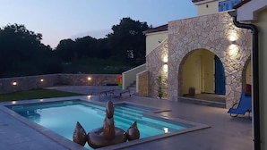 Une piscine bordée d’un mur en pierre et dotée d’une porte, entourée d’un patio aménagé avec des meubles d’extérieur.