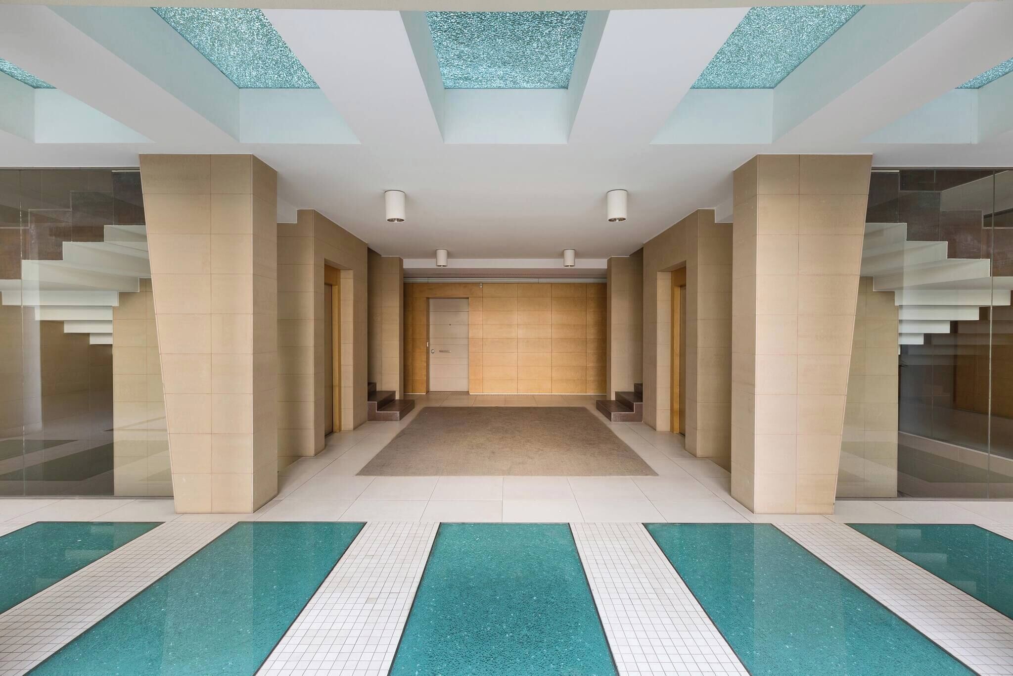 Eine moderne Hotelhalle mit einer zentralen Treppe, Glaswänden und einem Fliesenboden.