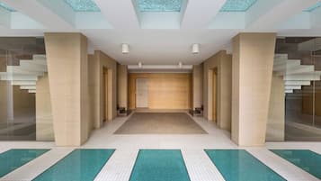 Eine moderne Hotelhalle mit einer zentralen Treppe, Glaswänden und einem Fliesenboden.