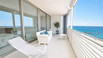 Ein Balkon mit weißem Sofa, einem kleinen Tisch und einem Stuhl mit Blick auf das Meer.
