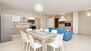A modern kitchen with white cabinets, a microwave, and a stove. There is a dining area with a table and chairs, and a blue sofa in the living room. - Apartment 5 Vele Sea View Free WIFI, 6 places (Gallipoli)
