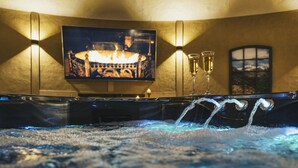 A hot tub with water jets, a television displaying a fireplace, and two lit candles. - Wellness-Speicher vacation apartment with sauna, whirlpool, breakfast and more (Freital)