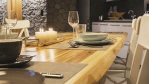 A dining table set with plates, glasses, and a candle, with a stone wall and kitchen in the background. - Wellness-Speicher vacation apartment with sauna, whirlpool, breakfast and more (Freital)
