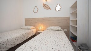 Une chambre avec deux lits, une tête de lit en bois, des appliques murales et une armoire blanche.