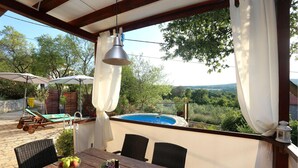 Un espace extérieur abrité comprenant une piscine, des chaises longues, une table avec un saladier de fruits et une vue sur le paysage environnant.