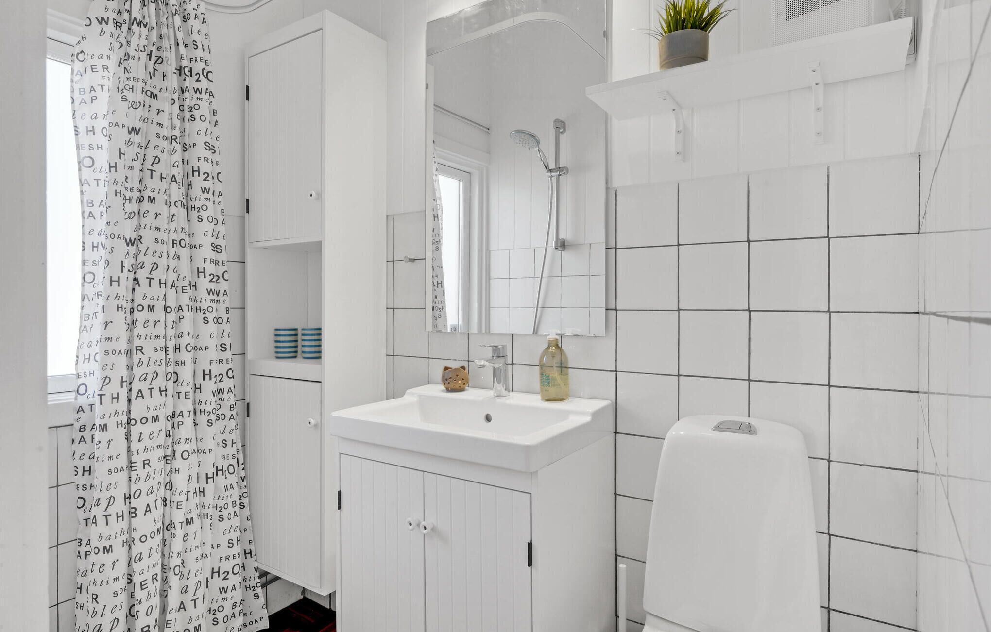 Ein modernes Badezimmer mit Waschbecken, Spiegel und Dusche. An der Wand steht ein Topf mit einer Pflanze und der Duschvorhang hat einen Aufdruck.