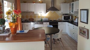 A kitchen with white cabinets, a black countertop, and a dining table with chairs. - Maison Vue mer avec grand jardin sur la Côte de Granit Rose (Pleumeur-Bodou)