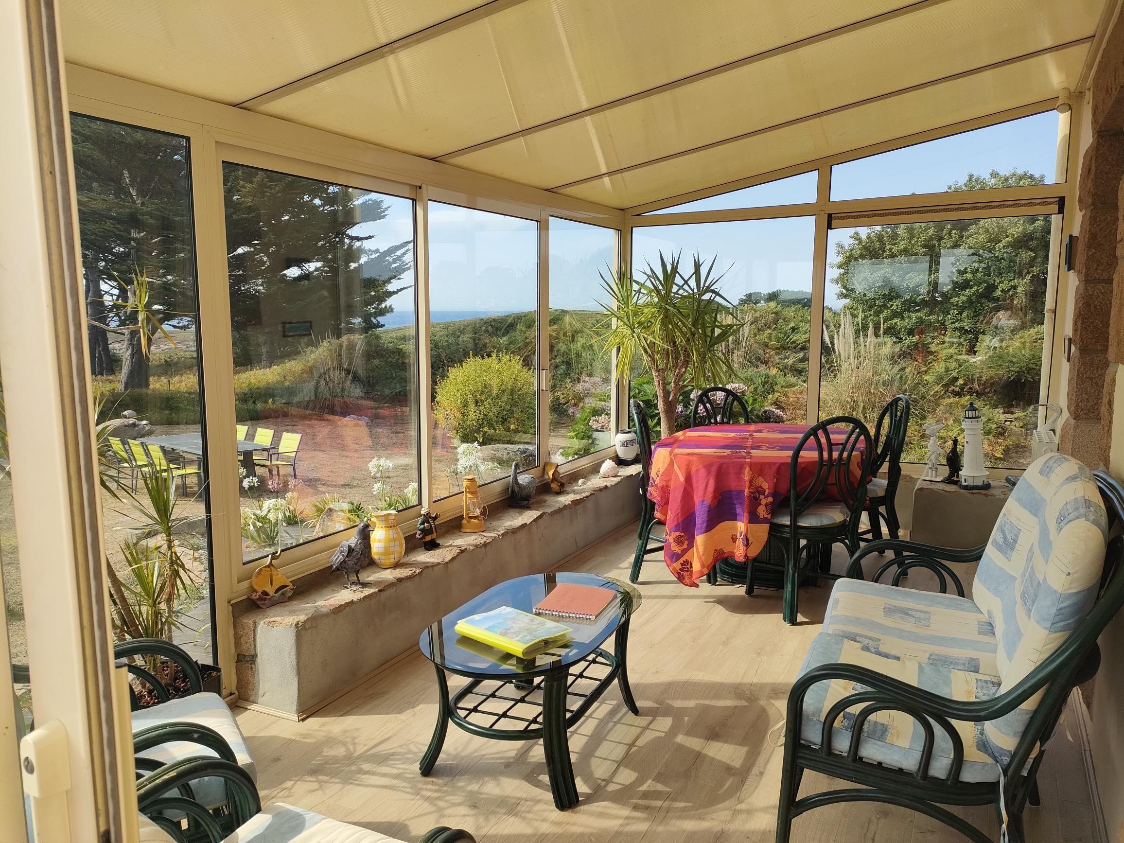 Un patio iluminado por el sol con una mesa y sillas, una mesa de cristal y vistas a un jardín y colinas.