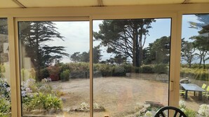 A room with a large sliding glass door leading to a garden with trees and plants. - Maison Vue mer avec grand jardin sur la Côte de Granit Rose (Pleumeur-Bodou)