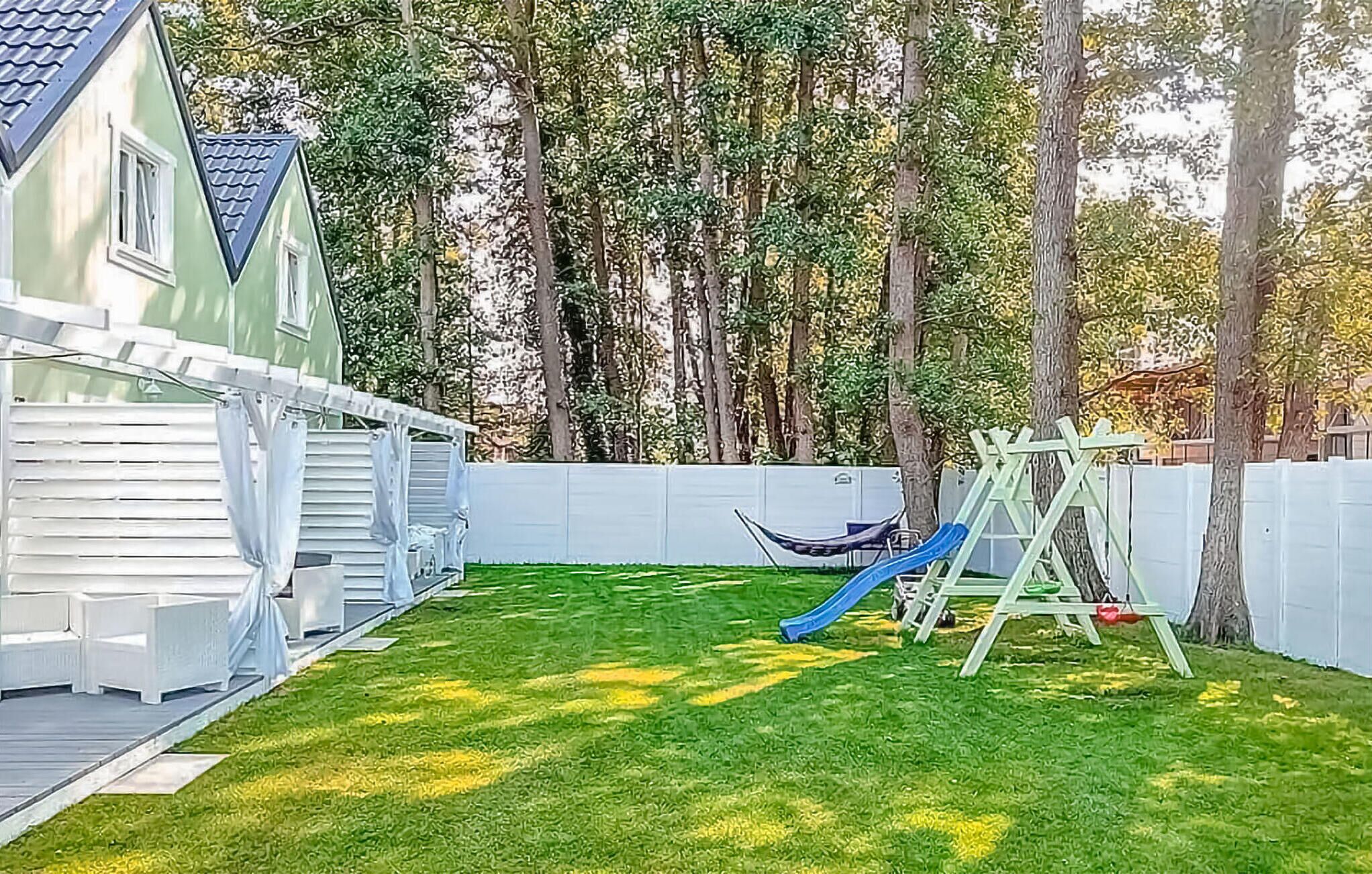 Un patio trasero con césped, un conjunto de columpios y una casita de juegos.