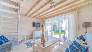 Un salon spacieux doté d’un plafond en bois, d’un téléviseur à écran plat, d’une commode blanche et d’une grande fenêtre donnant sur l’extérieur.