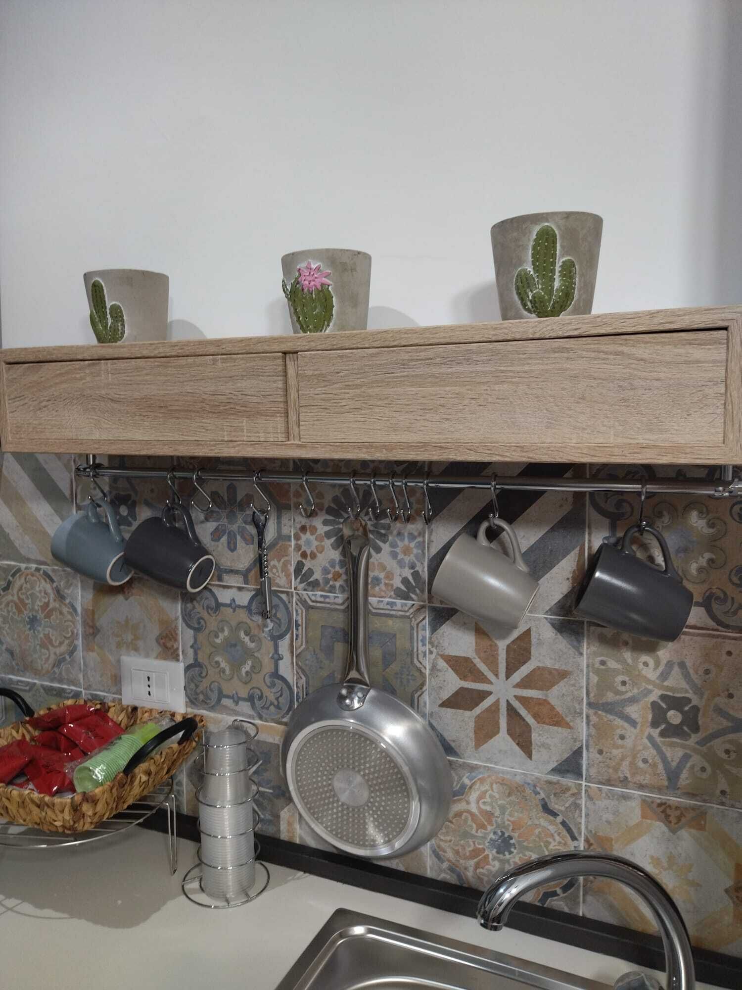 Een keuken met een houten aanrecht, hangende pannen, een metalen vergiet en een mand met groenten.