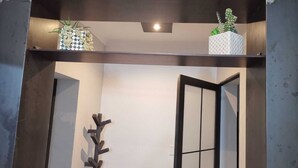 A modern interior with a dark wooden shelf holding decorative items, a wall-mounted abstract art piece, and a partially open door.