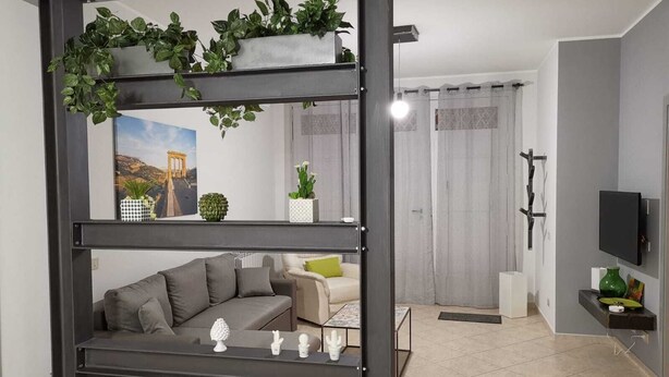 A modern living room with a sofa, a coffee table, and decorative items. There is a television mounted on the wall and a window with curtains.