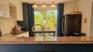 Una cocina con encimeras de granito, un lavamanos de acero inoxidable y un refrigerador. Hay una ventana con cortinas, un comedor con una mesa y sillas, y un letrero que dice 'Saint-Martin'.