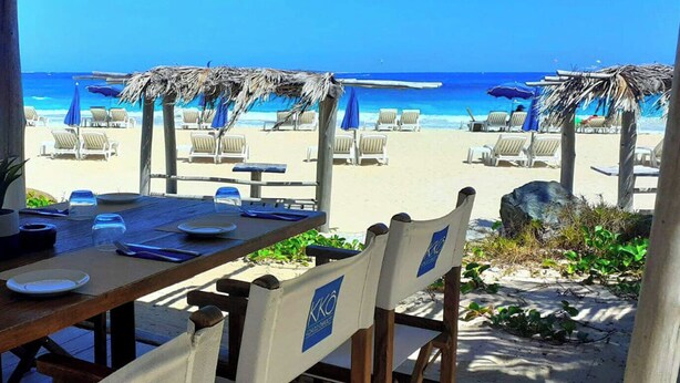 Un área de comedor frente a la playa con una mesa de madera preparada para dos personas, con vista al océano.