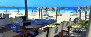 Un área de comedor frente a la playa con una mesa de madera preparada para dos personas, con vista al océano.