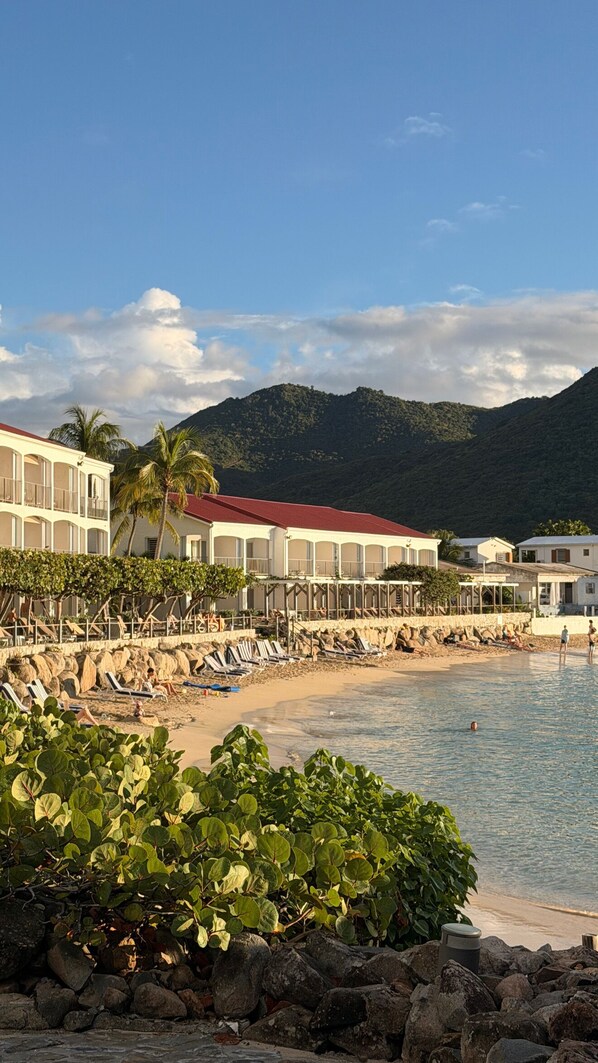 Un hotel frente a la playa con edificios de varios pisos, una playa de arena y un litoral rocoso.