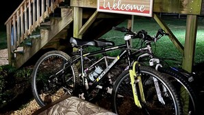 A wooden staircase with a 'Welcome' sign, a black bicycle, and a bench.