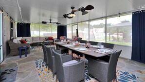 A covered patio area with a dining table set for four, surrounded by wicker chairs, and a sofa with cushions.