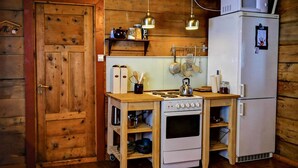 A compact kitchen with wooden cabinetry, a stove, a refrigerator, and hanging utensils.