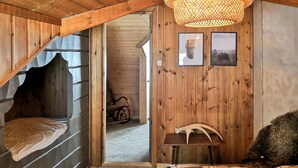 A cozy room with a sloped ceiling, a bed with a plaid blanket, a small wooden table, and a wall-mounted shelf.