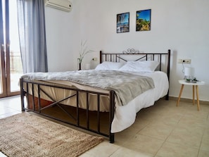 Ein Schlafzimmer mit einem Bett, einem kleinen Nachttisch, einer Wand-Klimaanlage und zwei gerahmten Bildern.