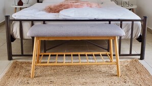 Un lit avec un banc devant, une table de chevet, une lampe et deux tableaux encadrés au mur.