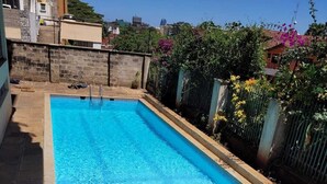 A rectangular swimming pool with clear blue water, surrounded by a tiled patio and a low stone wall. - Spacious 3 bedroom with pool (Nairobi)
