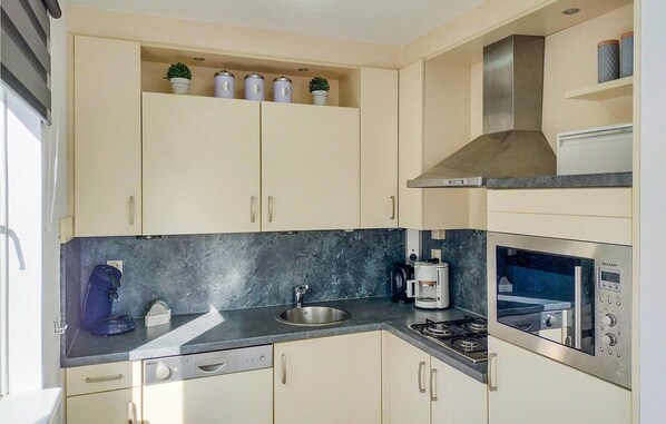 A modern kitchen with beige cabinets, a black countertop, a stainless steel sink, a coffee maker, and a built-in oven.