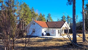 Ein eingeschossiges Haus mit roter Ziegeldach, umgeben von Bäumen und wolkenlosem, blauem Himmel.