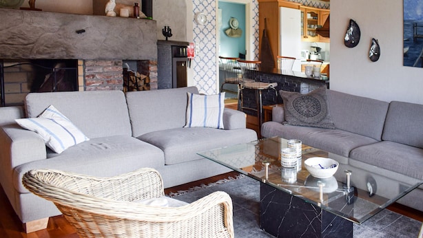 Ein Wohnzimmer mit zwei grauen Sofas, einem Korbsessel, einem Glastisch und einem Kamin.