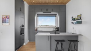 A modern kitchen with grey cabinets, a central island with bar stools, a window with a view, and a wooden ceiling. - 3 bedroom lovely home in Fjerritslev (Fjerritslev)