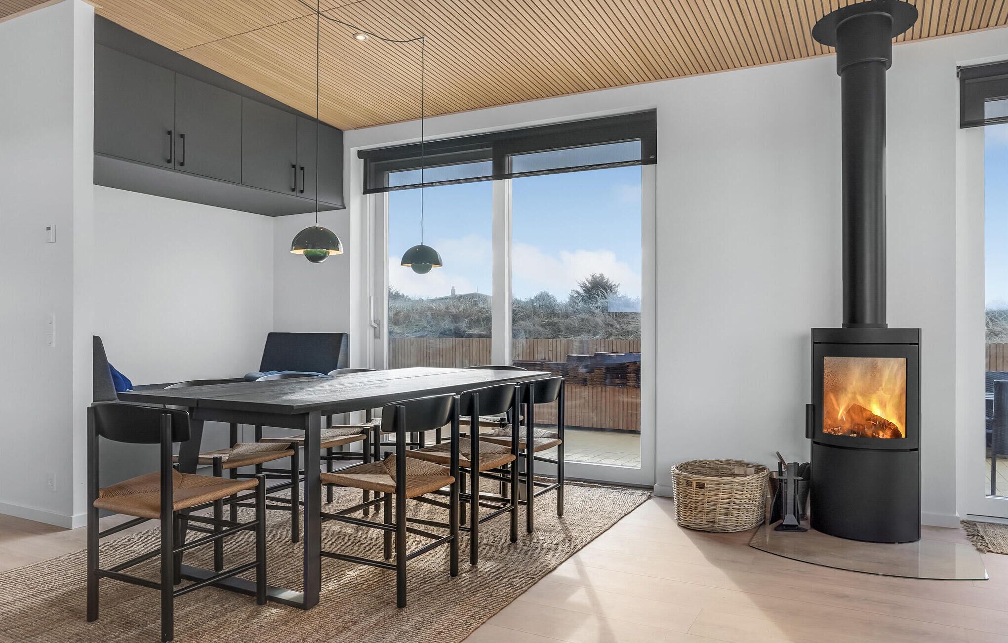 A modern kitchen with a large window, a dining area with chairs, and a wood-burning stove.