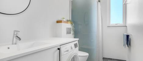 A compact bathroom with a white sink, a toilet, and a washing machine.