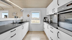 Eine moderne Küche mit weißen Schränken, Edelstahlgeräten und einem Fenster mit Blick ins Freie.