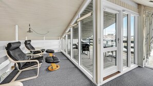 Ein überdachter Sitzbereich im Freien mit zwei Liegestühlen und einem kleinen Hocker, eine Glastür zum Außenbereich sowie eine Deckenleuchte.