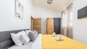 A hotel room with a bed, grey sofa, wooden wardrobe, and a TV on the wall. - Luxurious home in Pula (Pula)
