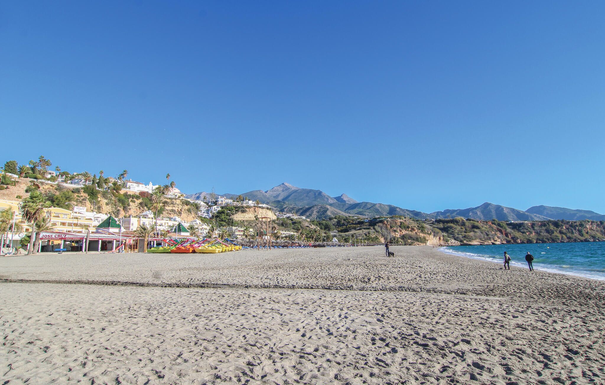 A beach with a clear sky, a sandy shore, and buildings in the background.