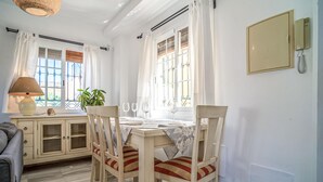 A dining area with a table set for two, two chairs, a lamp, and a potted plant.